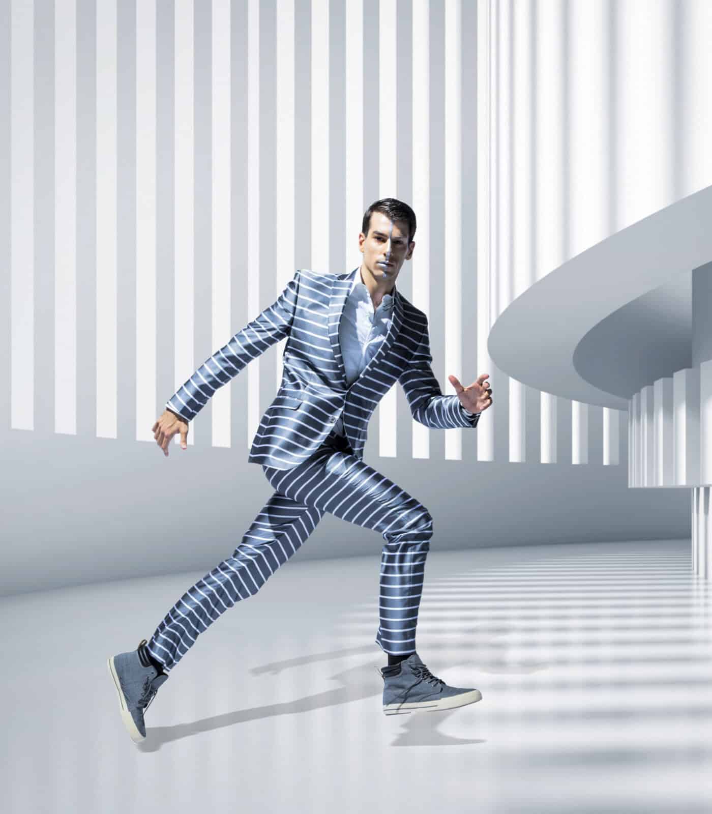 Man in a stylish striped suit walking confidently in a sleek, modern architectural environment.