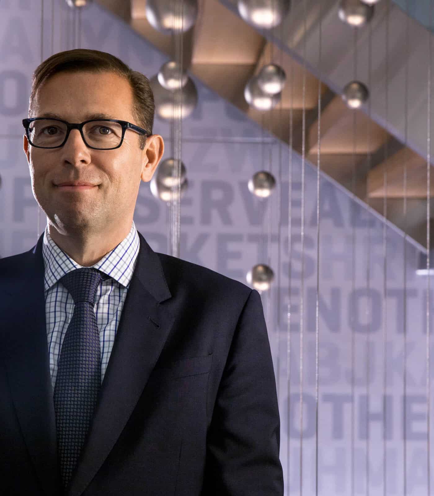 Businessman in a modern office setting with glass walls and stylish lighting fixtures.